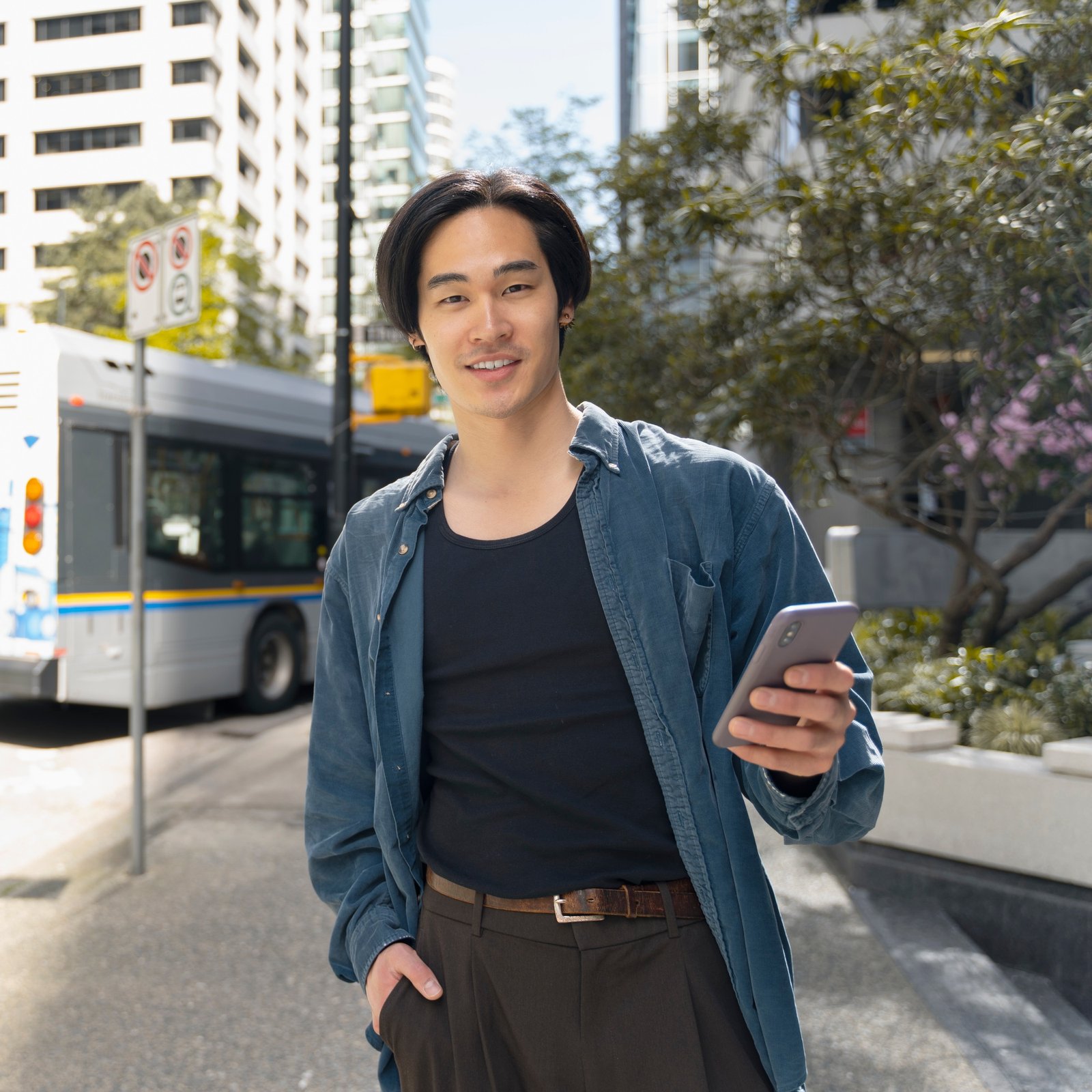 Portrait of handsome asian man holding mobile phone, looking at camera outdoors, on city street